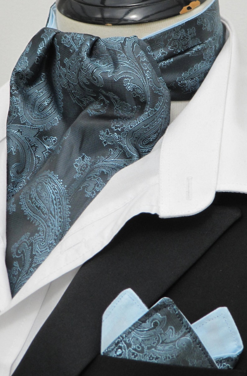 Op de afbeelding: Een zwarte en blauwe paisley-gepatroneerde das met een bijpassend zakdoekje. De das is om een witte overhemdkraag geknoopt.