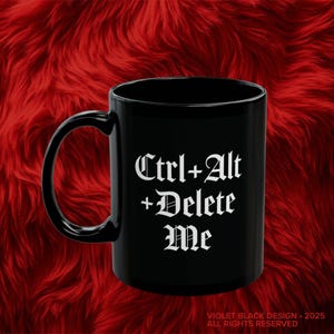 May include: Black ceramic mug with a curved handle. The mug features the text "Ctrl+Alt+Delete Me" in a gothic font. The mug is set against a red, textured background.