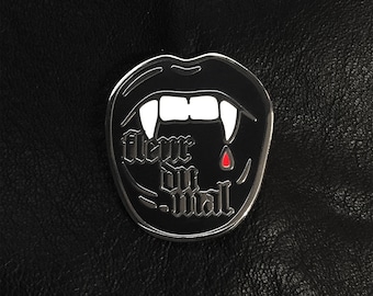 May include: A black enamel pin with a silver outline depicting a vampire's mouth with fangs and a drop of blood. The text "Never" and "Die" are visible inside the mouth.
