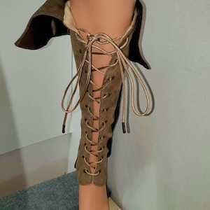 May include: Brown suede knee-high boots with lace-up detail and a fold-over top.