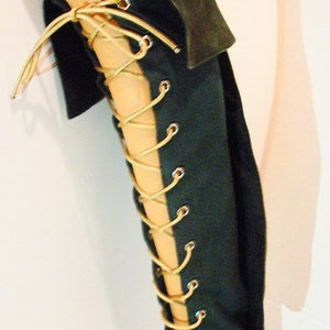 May include: A dark green leg wrap with a gold lace-up closure. The wrap is made of a soft, supple material and is designed to provide support and comfort.