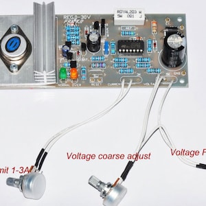May include: A silver circuit board with a black and white wire connected to a silver knob labeled "Voltage Fine Adjust". A second silver knob labeled "Voltage Coarse Adjust" is connected to the circuit board with a black and white wire. A third silver knob labeled "Current Limit 1-3A" is connected to the circuit board with a black and white wire. The circuit board has the text "REG.0-30V PRA-KIT" printed on it.