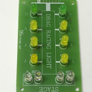 Può includere: Un circuito stampato verde con la scritta "DRAG RACING LIGHT" e "STAGE". Presenta diverse luci a LED: verdi, gialle e trasparenti. La scheda ha anche la scritta "VF FUTURE KIT".