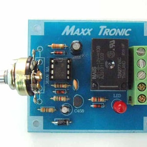 Op de afbeelding: Een blauwe printplaat met een zwarte relais, een groene klemmenstrook, een rode LED en een potentiometer met de aanduiding "VR 500K". Op de printplaat staat de tekst "MAXX TRONIC" gedrukt.