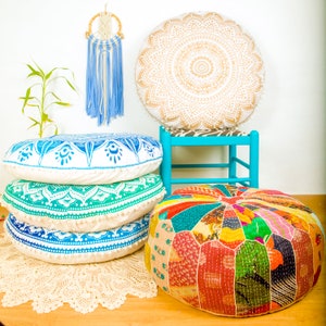 May include: Four round floor cushions in different patterns and colors. The cushions are arranged on a white rug with a blue and white dreamcatcher hanging above them. The cushions are made of fabric and have a variety of colors and patterns, including white, blue, green, and red.