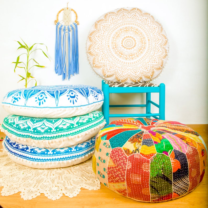 May include: Four round floor cushions in different patterns and colors. The cushions are arranged on a white rug with a blue and white dreamcatcher hanging above them. The cushions are made of fabric and have a variety of colors and patterns, including white, blue, green, and red.