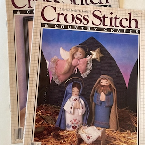May include: Two vintage "Cross Stitch & Country Crafts" magazines. The covers feature cross-stitched nativity scene figures: an angel, Mary, Joseph, and baby Jesus in a manger. The magazines have the text "22 Great Projects Inside!" and "32 Great Projects Inside!"
