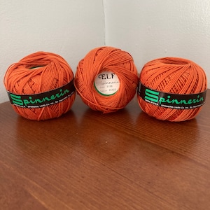 May include: Three orange yarn balls with the label "ELF Spinnerin" on one ball. The label includes the color number 5156 and dye lot 45422. The label also says "Made in USA Spinnerin Yarn Co. Inc."