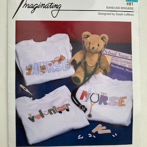 May include: A craft pattern titled "Band-Aid Brigade" featuring white sweatshirts with embroidered designs. One says "Nurse" with teddy bear accents, another says "Volunteer", and the third says "Nurse" with a stethoscope. A teddy bear with a stethoscope is also present.