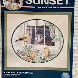May include: A Sunset counted cross-stitch kit titled "Charming Birdwatcher." The design features a cat looking out a window at birds. The kit includes cotton thread, aida cloth, a thread palette, needle, and instructions. The oval design measures 12" x 10" (30 x 25 cm).