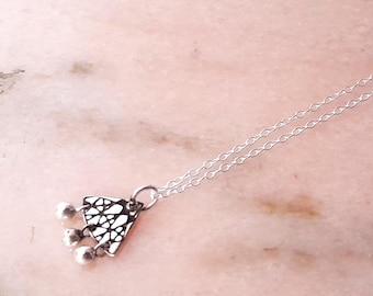 May include: A silver necklace with a small, ornate pendant featuring a triangular design and three dangling beads.
