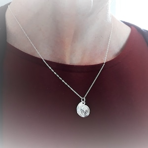 Peut inclure: Un collier en chaîne argent avec un pendentif rond en argent. Le pendentif a un design texturé.