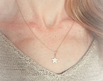 May include: A delicate gold chain necklace with a small star pendant. The necklace is worn by a person with long, light brown hair.