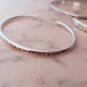 Peut inclure: Ensemble de trois bracelets ouverts en argent. Le bracelet avant présente un motif texturé sur le bord inférieur. Les bracelets sont présentés sur une surface en marbre rose et blanc. Bijoux.