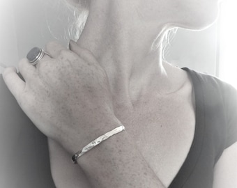May include: A silver hammered bangle bracelet on a person's wrist.