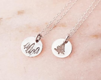 May include: Two silver necklaces with delicate chains and small round pendants. One pendant features a design of a group of trees, while the other pendant features a single tree design.