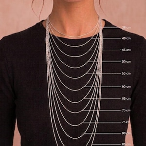 Op de afbeelding: Een reeks zilverkleurige metalen kettingen die om de hals worden gedragen, weergegeven in verschillende lengtes van 36 cm tot 90 cm. Elke ketting is gelabeld met de bijbehorende metrische lengte, wat een duidelijke visuele gids biedt voor maten.