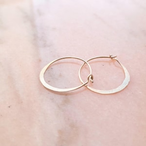 May include: A pair of gold hoop earrings with a hammered finish. The hoops are slightly curved and have a simple, minimalist design.