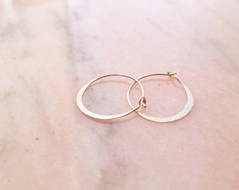 May include: A pair of thin, circular gold hoop earrings with a delicate wire construction and a simple hook closure mechanism. The earrings feature a smooth, polished metallic finish that reflects light, creating a subtle shine across the surface.
