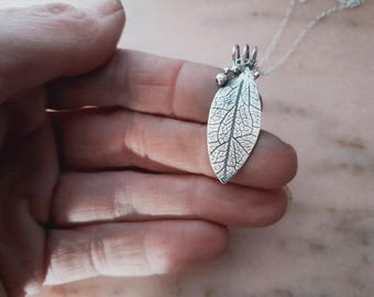May include: A silver necklace with a leaf pendant and small silver beads. The leaf is detailed with veins and has a textured surface.