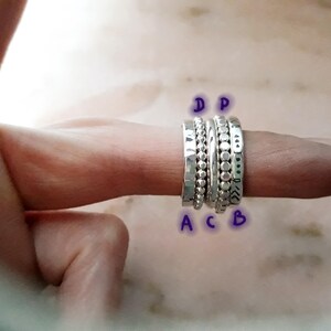 May include: A selection of silver rings displayed on a finger. The rings showcase diverse designs, such as hammered textures, beaded details, and dotted patterns. The rings are set against a soft, blurred background.