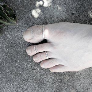 Puede incluir: Cuatro anillos de plata para los dedos del pie en un pie. Los anillos están apilados en el segundo dedo del pie.