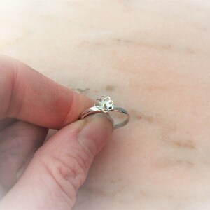 May include: A silver ring featuring a flower design. The ring is held in a hand, highlighting the floral detail. The ring's band is slender and polished, and the flower has multiple petals. The ring is a piece of jewellery.