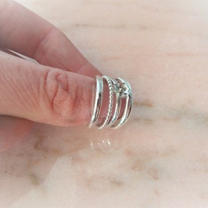 May include: A set of four silver rings. One ring is a solid band, another has a beaded design, and the third features a floral design. The rings are worn together on a finger.