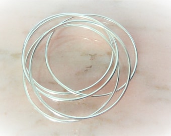 May include: A set of five silver bangle bracelets, stacked and overlapping, on a pink background.