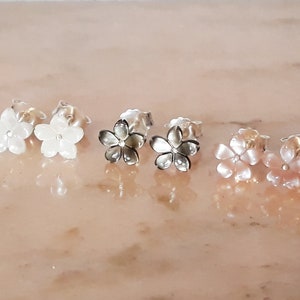 Peut inclure: Trois paires de boucles d'oreilles en forme de fleur. La première paire est blanche, la deuxième paire est grise et la troisième paire est rose.