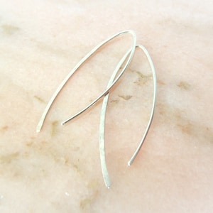 May include: A pair of silver hammered hoop earrings. The earrings are thin and delicate, with a slightly curved shape.