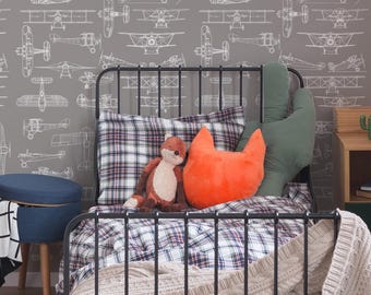 May include: A child's bedroom with a black metal bed frame, plaid bedding, and decorative pillows. A stuffed fox and an orange fox-shaped pillow are on the bed. The gray wall features a white airplane pattern. A blue ottoman is on the left.