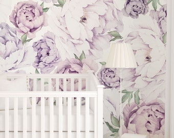 Könnte beinhalten: Ein weißes Babybett mit einem weißen Rüschenrock und einem weißen Kissen. Das Babybett steht vor einer Wand mit einer floralen Tapete mit großen lila und weißen Pfingstrosen.