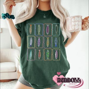 May include: A dark green t-shirt with a colorful fish design. The fish are arranged in a grid pattern and are outlined in black. The shirt has a crew neck and short sleeves.