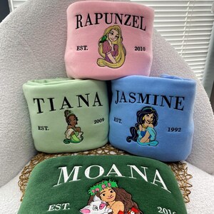 Może przedstawiać: Cztery haftowane polarowe koce z księżniczkami Disneya: Roszpunką, Tianą, Jaśminą i Moaną. Każdy koc jest w innym kolorze: r&oacute;żowym, zielonym, niebieskim i ciemnozielonym. Każdy koc ma imię księżniczki, obraz i rok założenia.