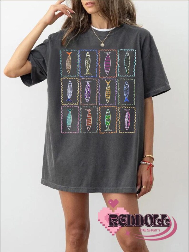 May include: A charcoal gray oversized t-shirt with a graphic print of a grid of colorful fish in frames.