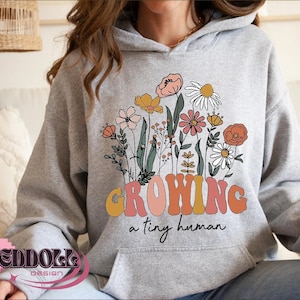 May include: Gray hooded sweatshirt with a floral design and the text "Growing a tiny human".
