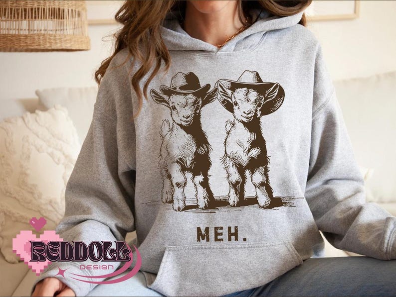 K&ouml;nnte beinhalten: Grauer Hoodie mit einem Aufdruck von zwei Ziegen, die Cowboyh&uuml;te tragen. Die Ziegen sind braun und wei&szlig; und der Text "MEH." ist darunter gedruckt.