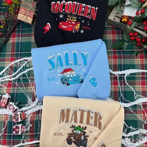 Puede incluir: Tres sudaderas plegadas con personajes de la pel&iacute;cula Cars. La sudadera superior es negra con "McQueen" en rojo y un gr&aacute;fico de coche rojo. La sudadera del medio es azul claro con "Sally" en blanco. La sudadera inferior es beige con "Mater" en marr&oacute;n.