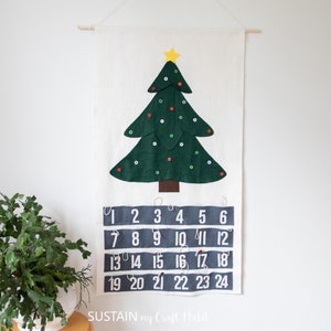 May include: A felt Christmas tree advent calendar with a green tree, a yellow star, and red and white buttons. The numbers 1 through 24 are printed in white on a gray background.
