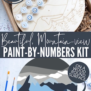 Peut inclure: Un kit de peinture par num&eacute;ros repr&eacute;sentant un paysage de montagne avec des couleurs bleues, grises et vertes. Le kit comprend une surface ronde en bois, des pots de peinture et des pinceaux. Le texte "PIN ME!" et "Beautiful, Mountain-view PAINT-BY-NUMBERS KIT" est visible sur l'image. Le texte "ON A WOOD ROUND SURFACE" est &eacute;galement visible.