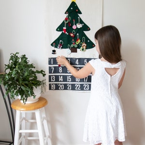 May include: A felt Christmas tree advent calendar with 23 numbered pockets and a felt star on top. A child is opening a pocket on the calendar.