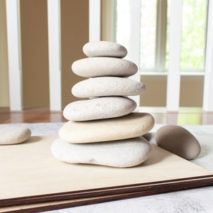 May include: A stack of smooth, gray and white stones balanced on top of each other. The stones are arranged in a pyramid shape, with the largest stone at the bottom and the smallest stone at the top.