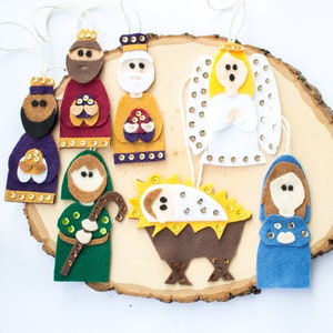 May include: Felt Christmas ornaments depicting the Nativity scene. The ornaments include a shepherd, three wise men, an angel, Mary, Joseph, and baby Jesus in a manger.
