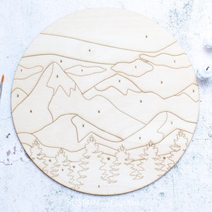Peut inclure: Un kit de peinture par num&eacute;ros en bois repr&eacute;sentant un paysage de montagne avec des arbres. Le kit comprend des pots de peinture num&eacute;rot&eacute;s de 1 &agrave; 10 et deux pinceaux.
