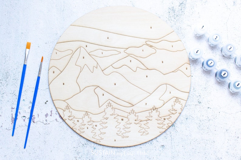 Peut inclure: Un kit de peinture par num&eacute;ros en bois repr&eacute;sentant un paysage de montagne avec des arbres. Le kit comprend des pots de peinture num&eacute;rot&eacute;s de 1 &agrave; 10 et deux pinceaux.