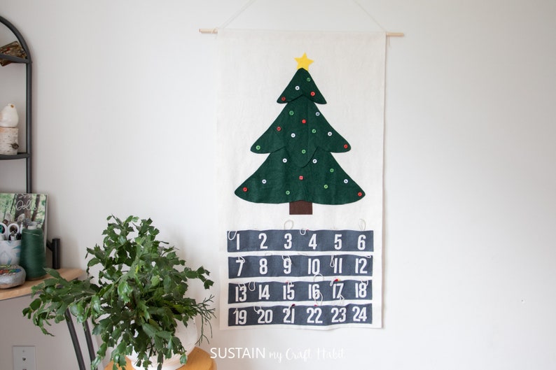 May include: A felt Christmas tree advent calendar with a green tree, a yellow star, and red and white buttons. The numbers 1 through 24 are printed in white on a gray background.
