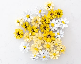 Puede incluir: Un grupo de piñas pintadas de blanco y amarillo, dispuestas para parecer flores. Las piñas están pintadas en tonos de blanco, amarillo y crema.