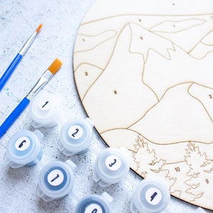 Peut inclure: Un kit de peinture par num&eacute;ros avec une toile en bois, des pots de peinture et des pinceaux. La toile pr&eacute;sente un motif de montagnes et d'arbres. Les pots de peinture sont num&eacute;rot&eacute;s de 1 &agrave; 10.