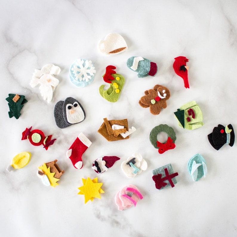 May include: A set of felt Christmas ornaments in various shapes and colors, including a penguin, a snowman, a gingerbread man, a Christmas tree, a stocking, a candy cane, a wreath, a star, a bell, a cardinal, a snowflake, a Santa hat, and a present.